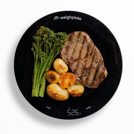 Black Weighplate smart plate showing grilled steak, potatoes and greens with a digital weight reading on the plate.